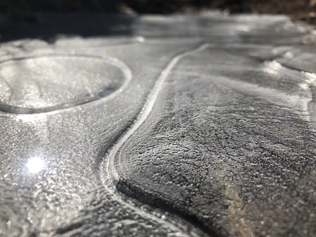 A frozen creek, the ice has interesting textures and sunlight is reflecting on the surface ￼