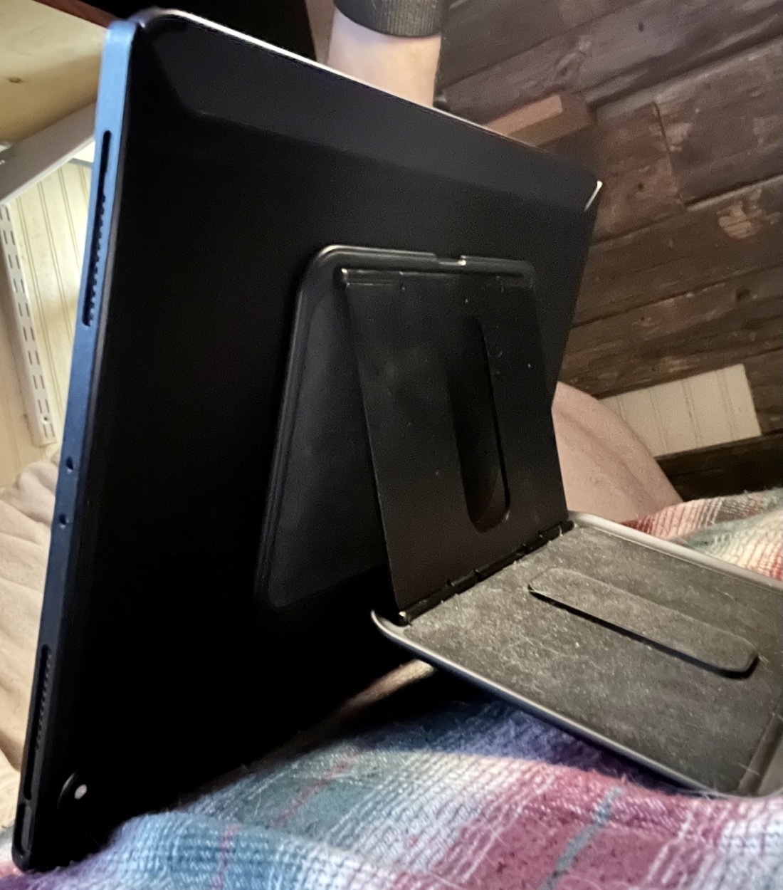An iPad with an adjustable kickstand attached to the back via a magnet. The iPad is resting on a pillow.