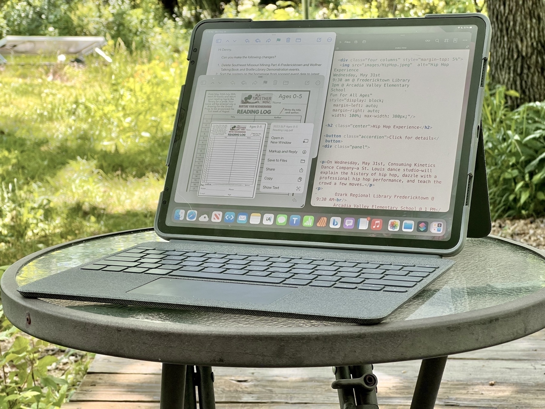 Photo of an iPad sitting on a glass topped table. The photo is taken outside against a blurred green background